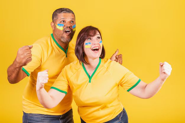 Two excited soccer fans in yellow jerseys with face paint cheering against a yellow background.